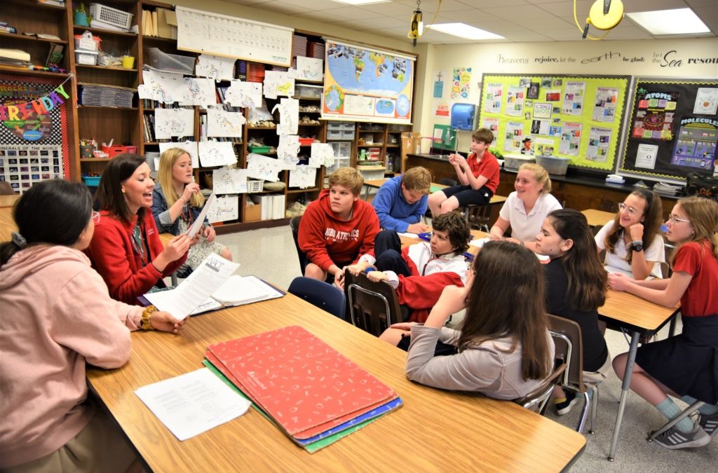 A teacher with students sitting around a table in a classroom at River Oaks Baptist School