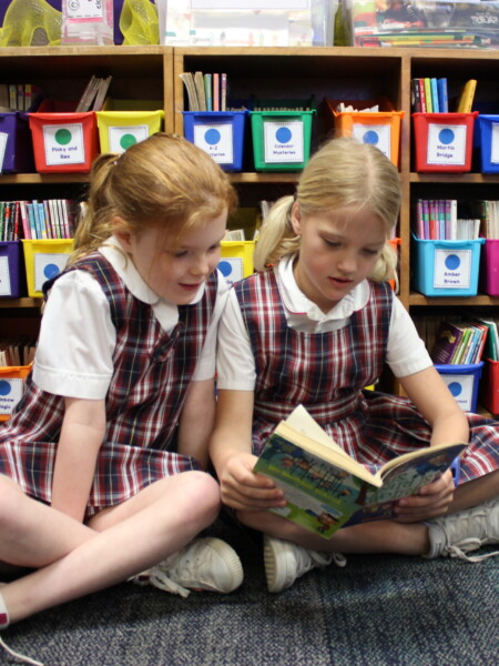 Two girls, students of River Oaks Baptist School, sitting on the floor reading a book