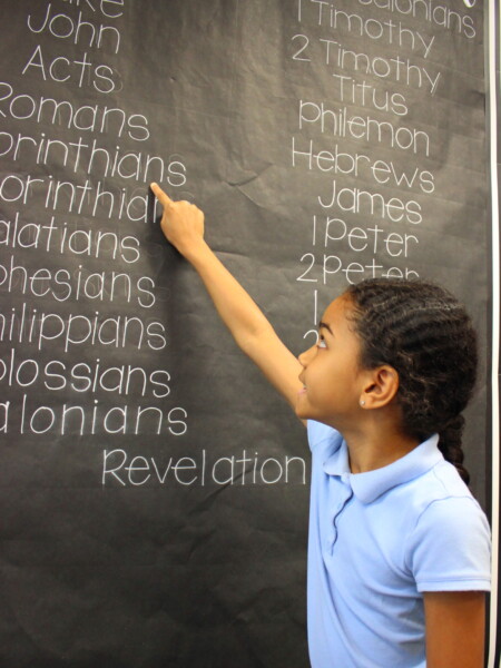 A young girl writing on a blackboard in a classroom at River Oaks Baptist School