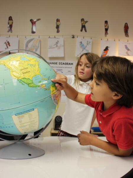 A couple of kids looking at a globe learning in a classroom