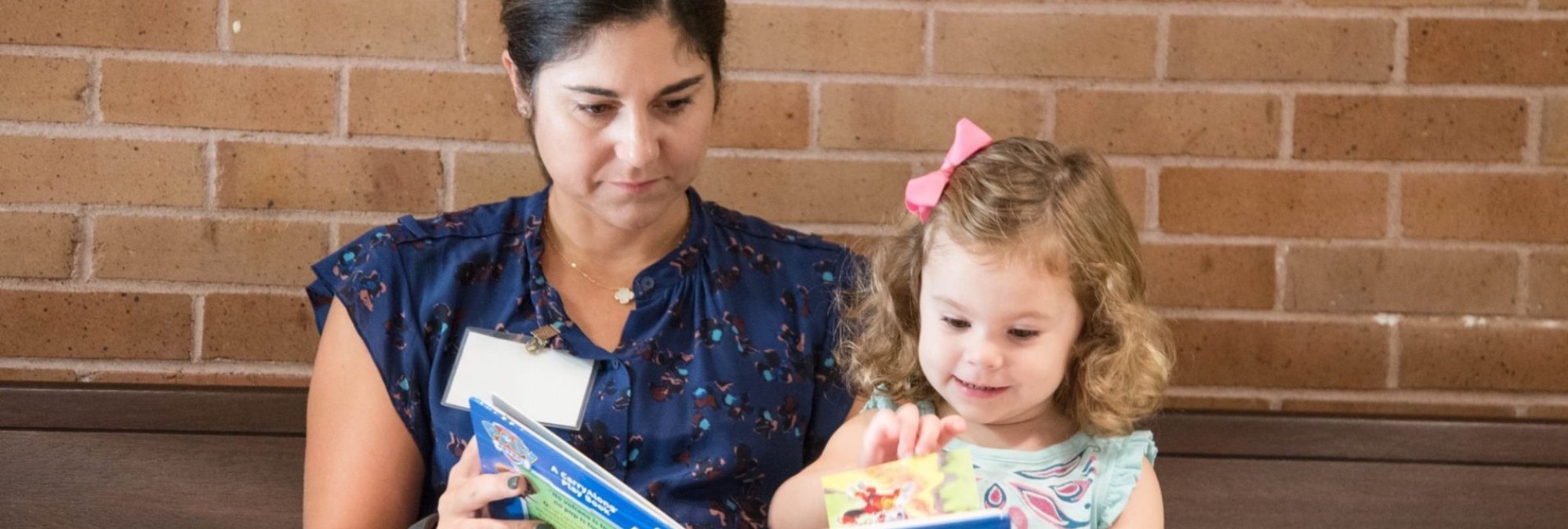 A teacher reading a book to a little girl at River Oaks Baptist School