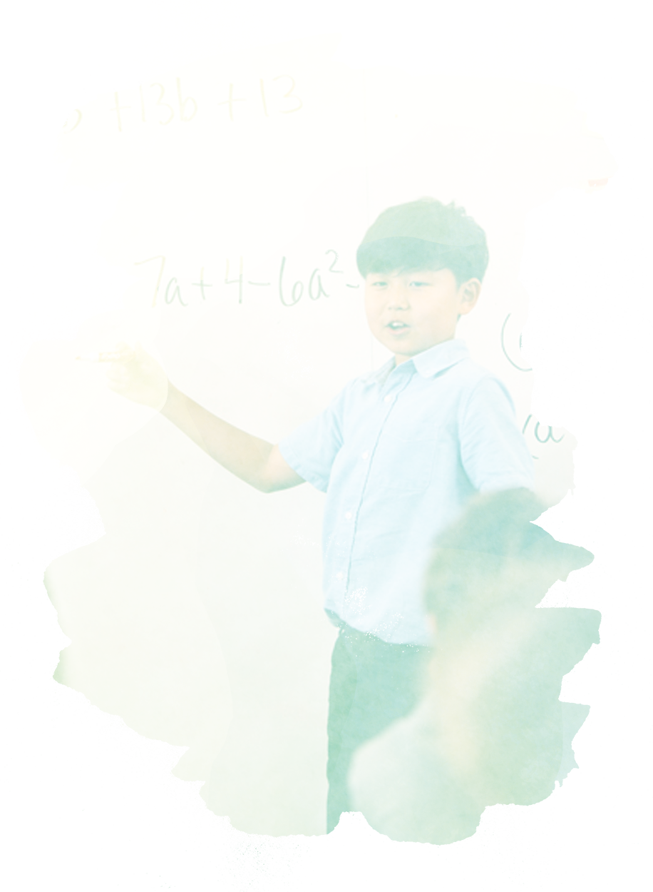 A boy standing in front of a whiteboard with writing on it in a classroom