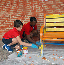 A kid learning to paint a bench with a teacher at River Oaks Baptist School