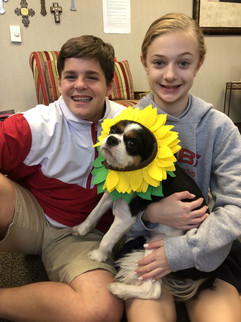 A boy and a girl sitting on a couch with a dog wearing a sunflower at River Oaks Baptist School