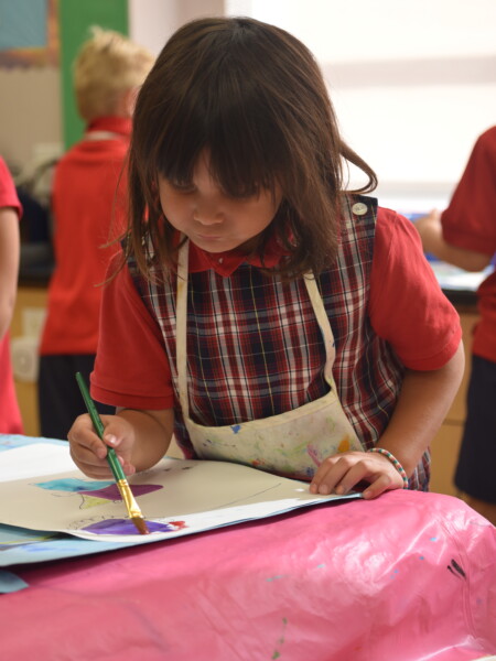 A young girl in a red shirt painting in a classroom