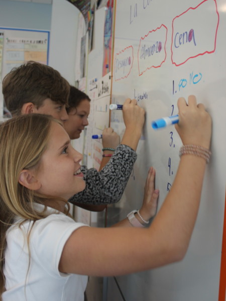 A group of children writing on a whiteboard in a classroom