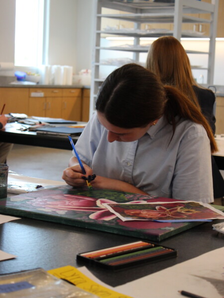 A girl student sitting at a table working on a painting at River Oaks Baptist School