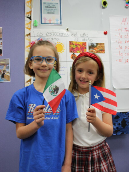 Two young girls holding flags in front of a bulletin board at River Oaks Baptist School