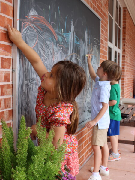 Two children drawing on a blackboard on a brick wall at River Oaks Baptist School
