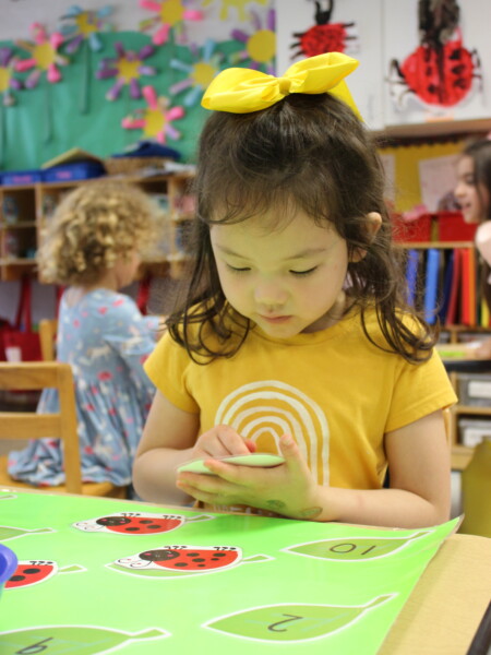A little girl sitting at a table pasting a ladybug picture in a classroom