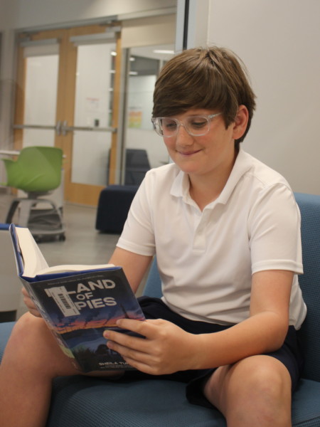 A boy sitting on a couch reading a book in a classroom