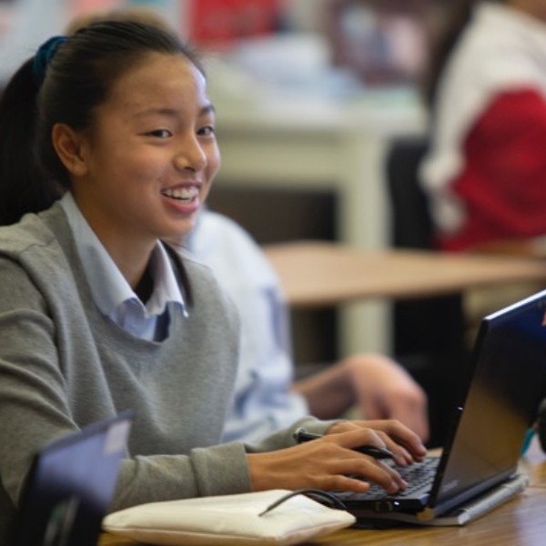 A girl smiles while using a laptop computer at River Oaks Baptist School
