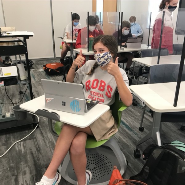 A student with mask on the face sitting at a table with a laptop at River Oaks Baptist School