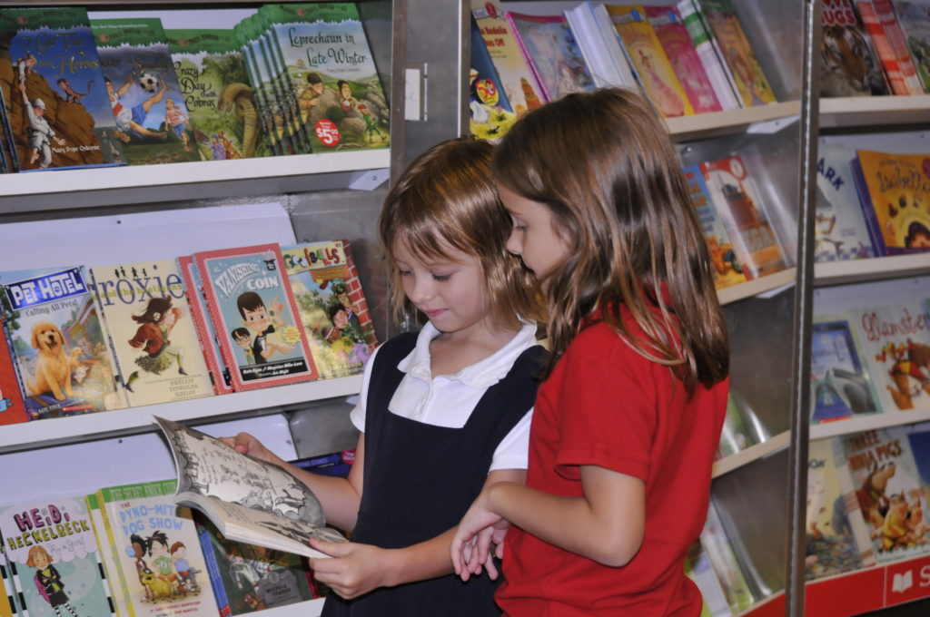 Two little girls students are looking at books in a library at River Oaks Baptist School