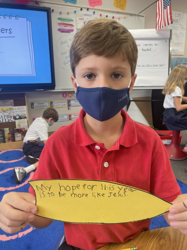 A boy student in a red shirt holding a piece of paper with the quote "My hope for this year is to be more like Jesus"