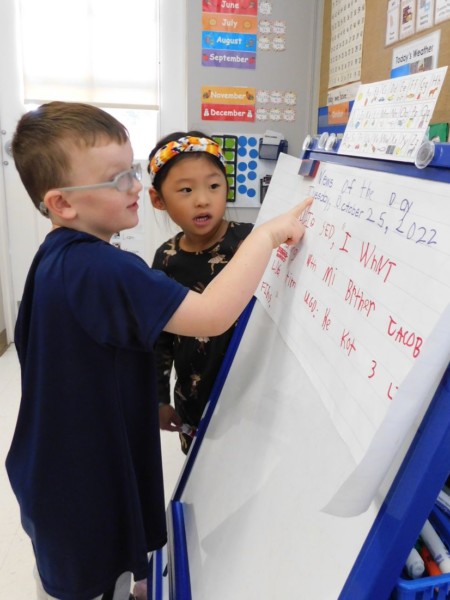 Two students reading on a whiteboard in a classroom