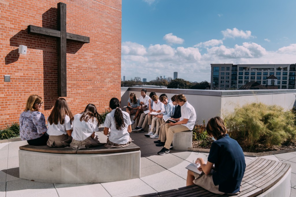 A group of people sitting on a bench in front of a cross at River Oaks Baptist School