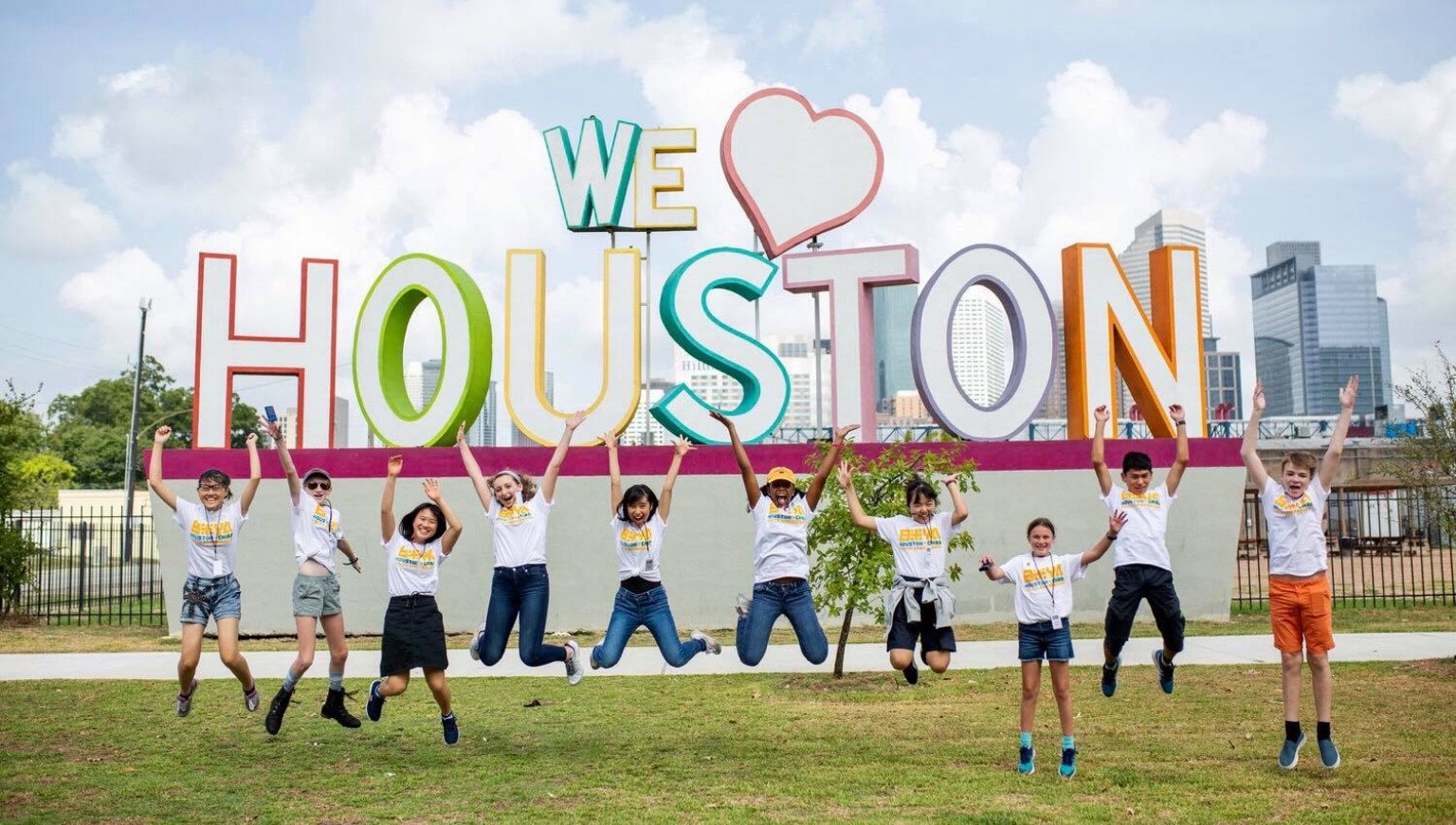 A group of students of ROBS jumping in the air in front of a "We Love Houston" sign
