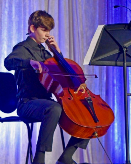 A young man sitting on a chair playing a cello at River Oaks Baptist School