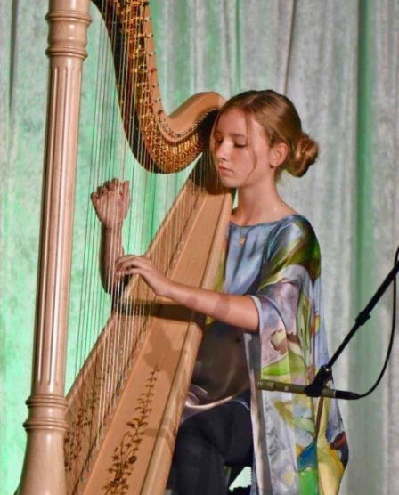 A woman playing a harp on a stage at River Oaks Baptist School