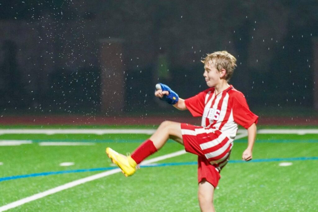 A young boy student kicking a soccer ball on a field at River Oaks Baptist School