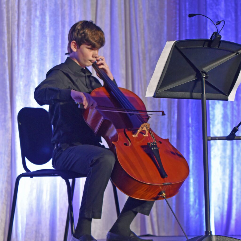 A young student sitting on a chair playing a cello at River Oaks Baptist School