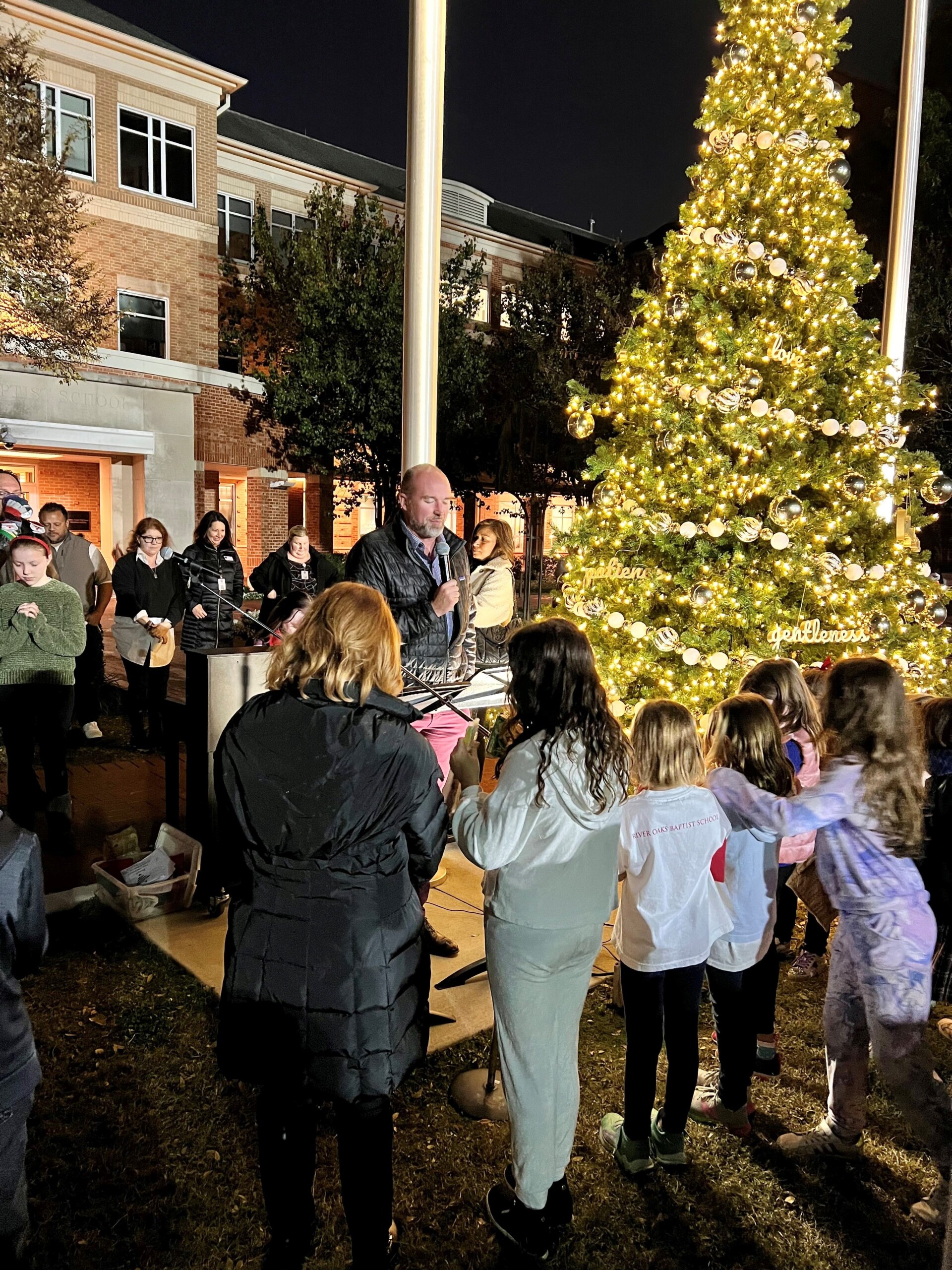 A group of people standing around a Christmas tree at River Oaks Baptist School